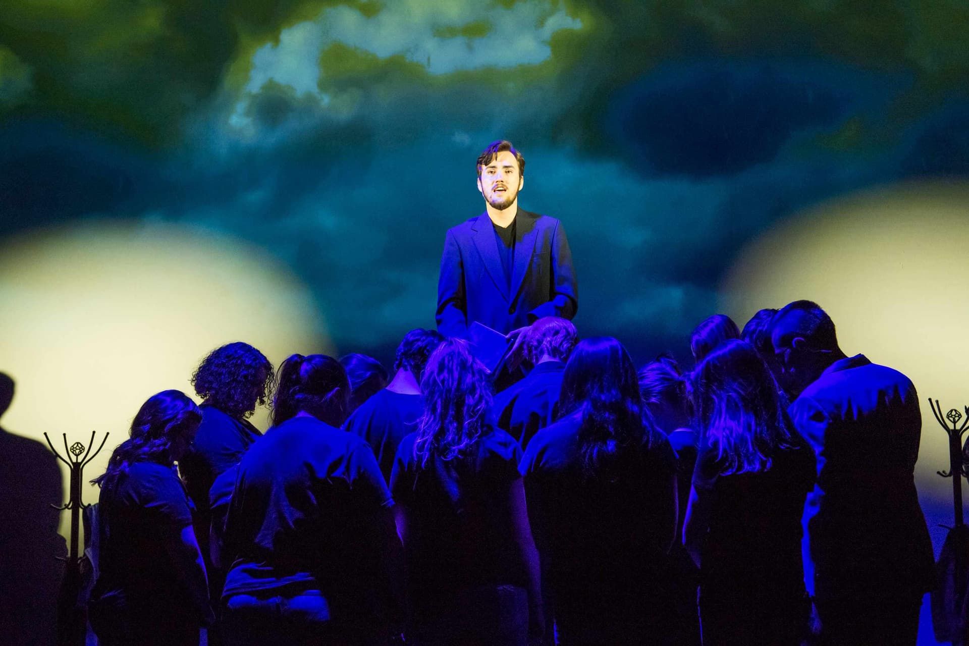 Soloist performing above the ensemble in dramatic blue light