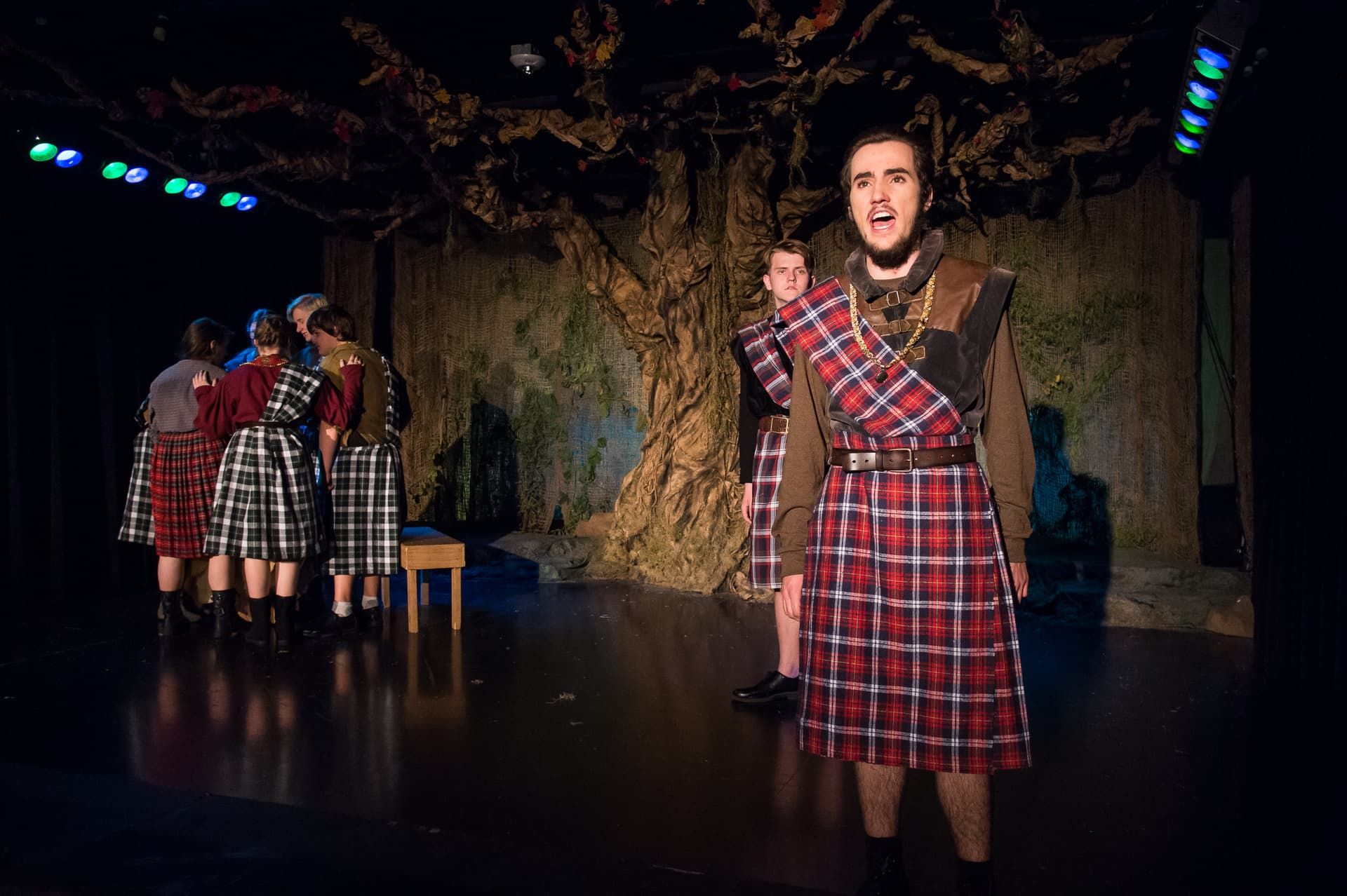 A kilted student performs a monologue on the forest set of Macbeth